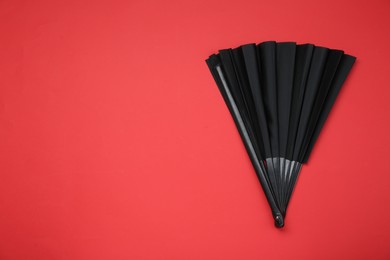 Photo of Stylish black hand fan on red background, top view. Space for text