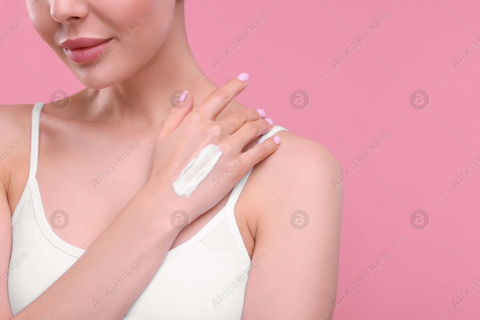 Photo of Woman with smear of body cream on her hand against pink background, closeup. Space for text