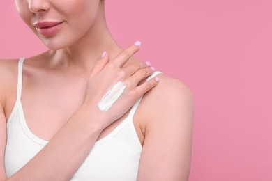 Photo of Woman with smear of body cream on her hand against pink background, closeup. Space for text