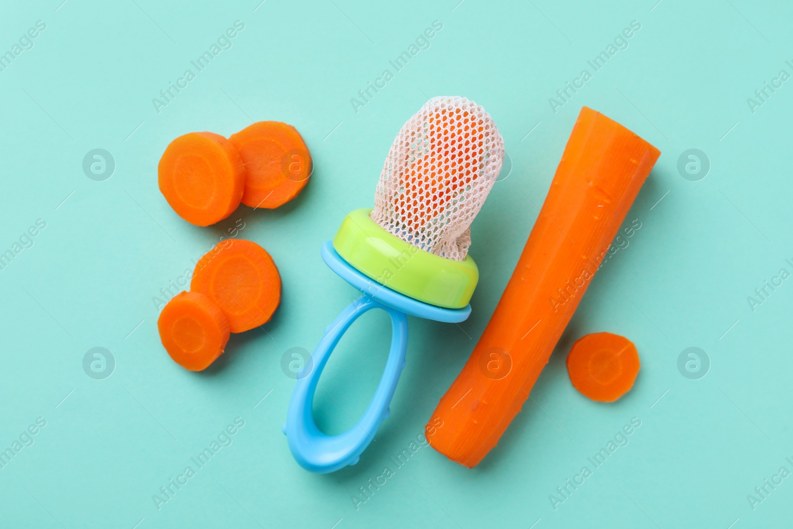 Photo of Nibbler with boiled carrot on turquoise background, flat lay. Baby feeder