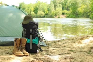 Modern camping tent and equipment on riverbank. Space for text