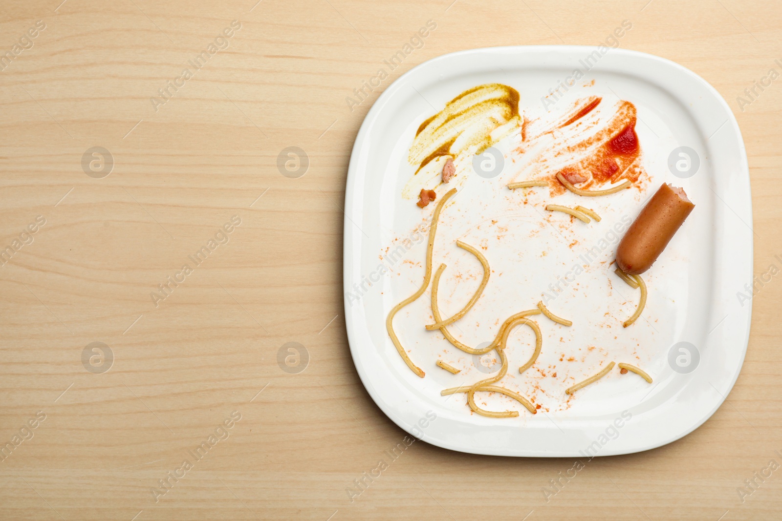 Photo of Dirty plate with food leftovers and sausage on wooden background, top view. Space for text