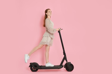Photo of Happy woman riding modern electric kick scooter on pink background