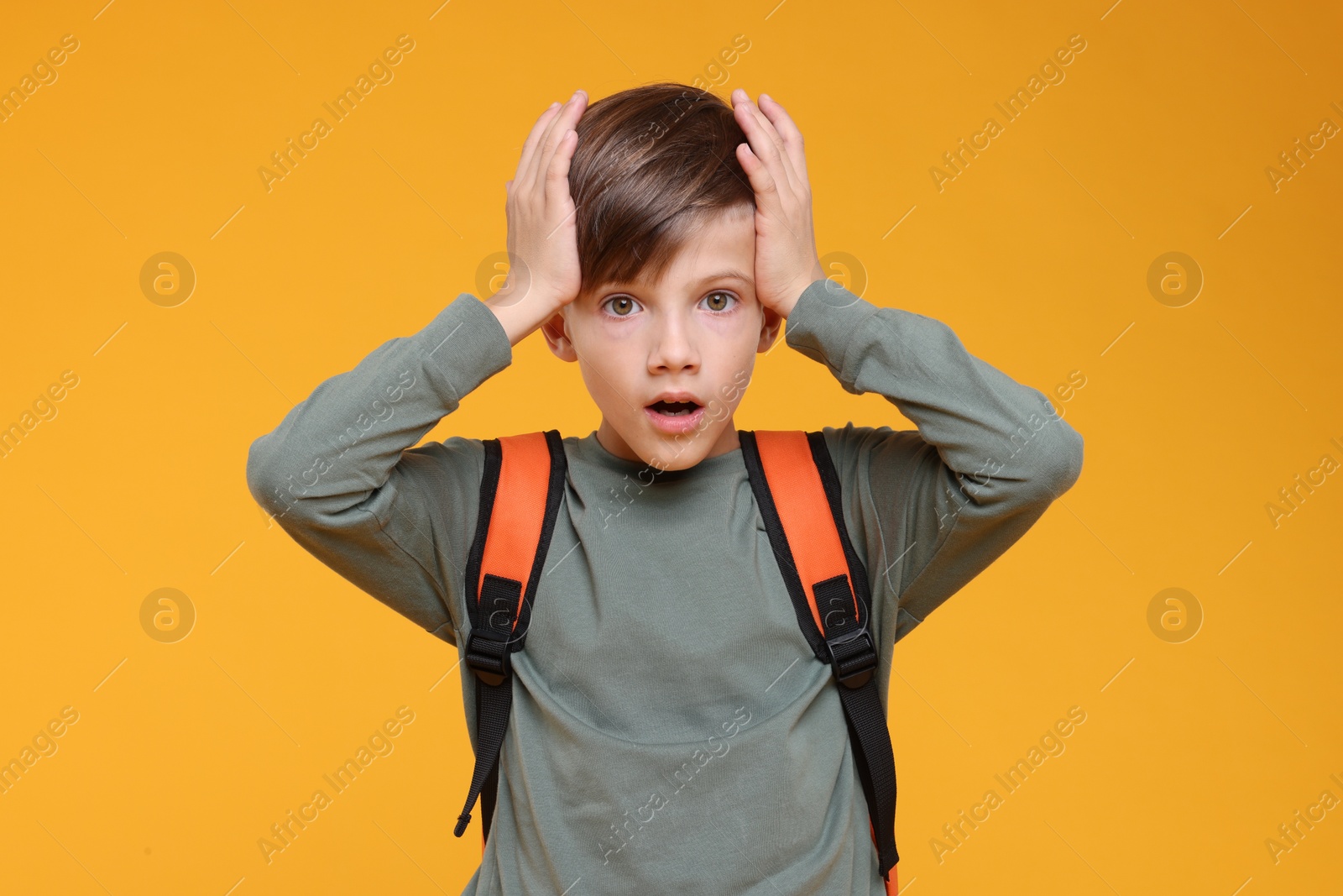 Photo of Surprised schoolboy covering head with hands on orange background
