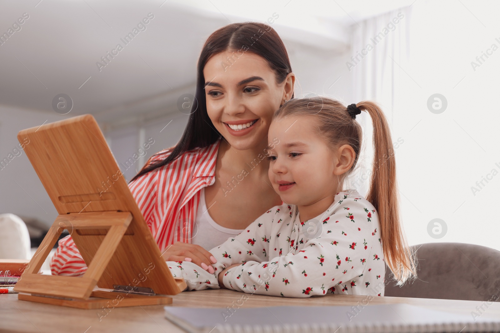 Photo of Mother helping her daughter with homework using tablet at home