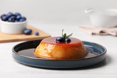 Photo of Plate of delicious caramel pudding with blueberries and mint on white wooden table