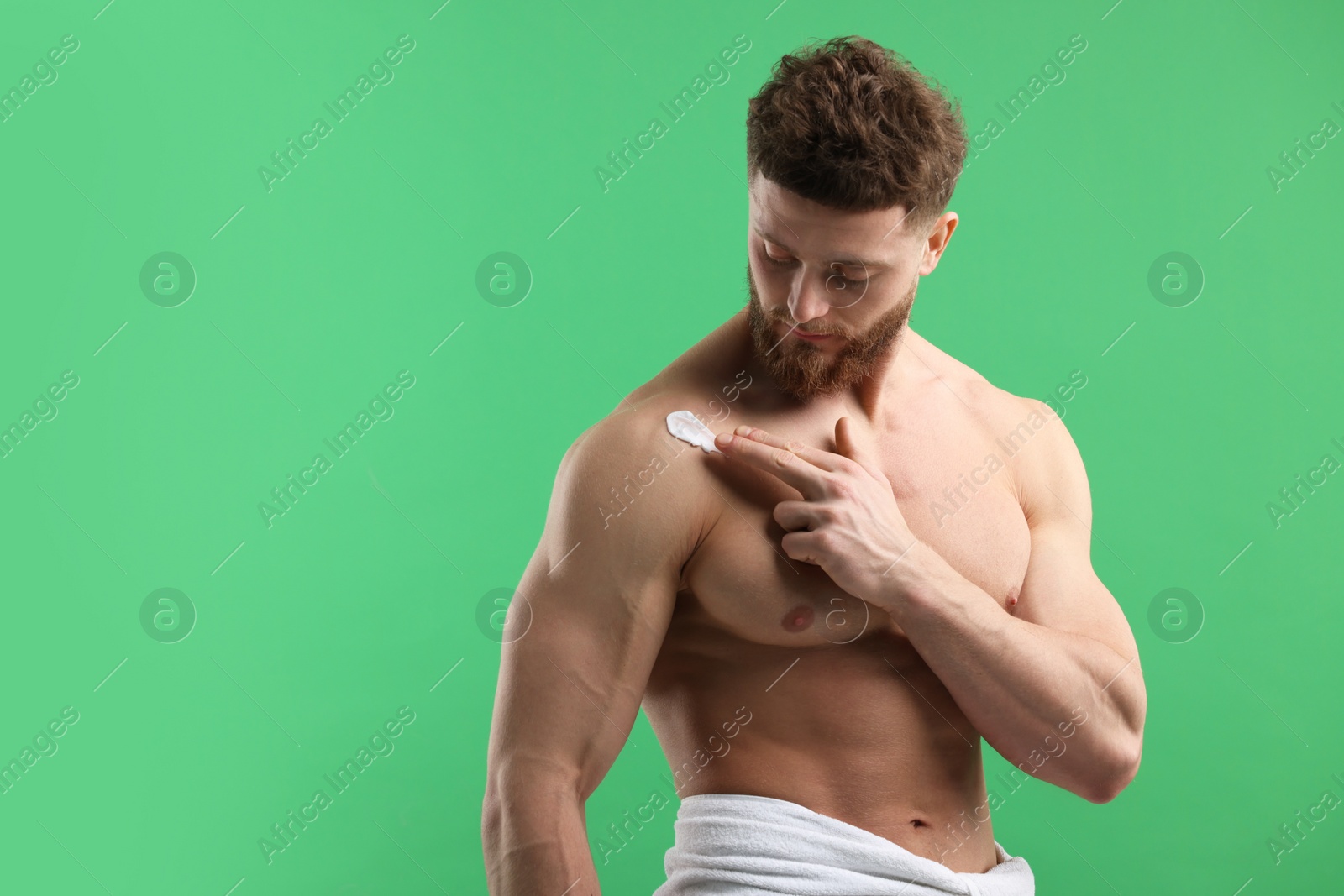 Photo of Handsome man applying moisturizing cream onto his shoulder on green background, space for text