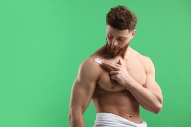 Handsome man applying moisturizing cream onto his shoulder on green background, space for text