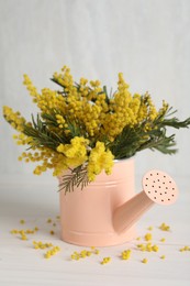 Beautiful mimosa flowers in watering can on white wooden table