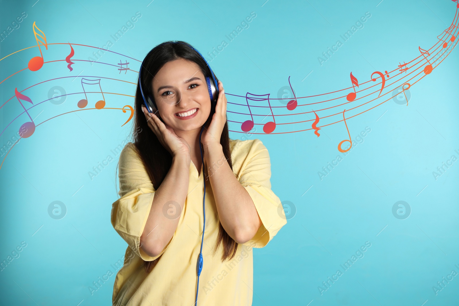 Image of Attractive woman listening to music via headphones on light blue background