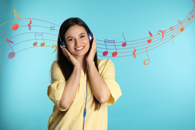 Attractive woman listening to music via headphones on light blue background