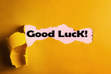 Image of Phrase GOOD LUCK on pink background, view through hole on yellow paper