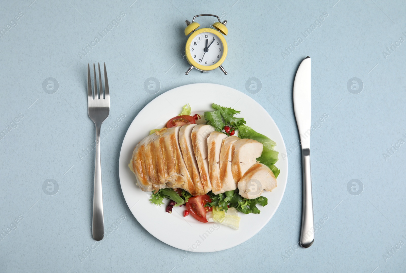 Photo of Plate of appetizing food, alarm clock and cutlery on light blue table, flat lay. Nutrition regime