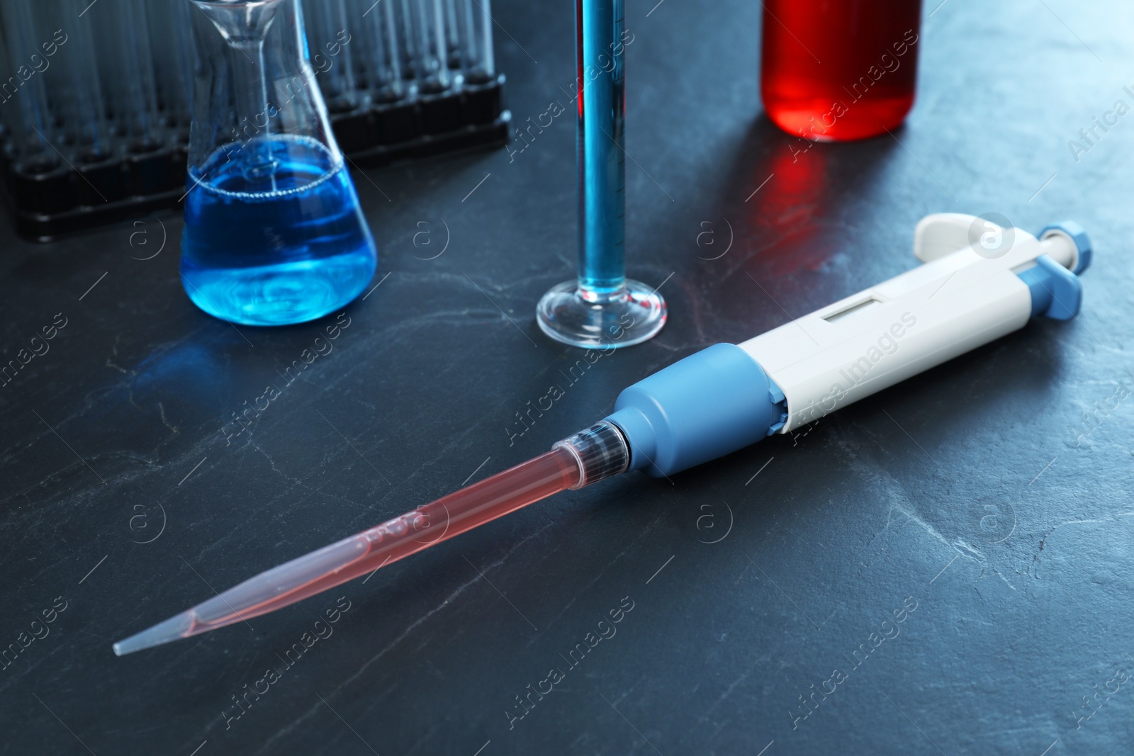 Photo of Laboratory analysis. Micropipette and different glassware on black table, closeup