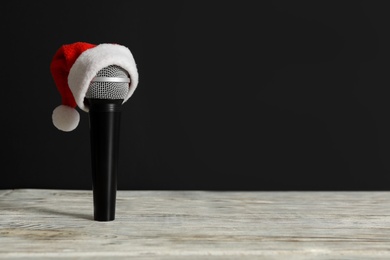 Microphone with Santa hat on white table against black background, space for text. Christmas music