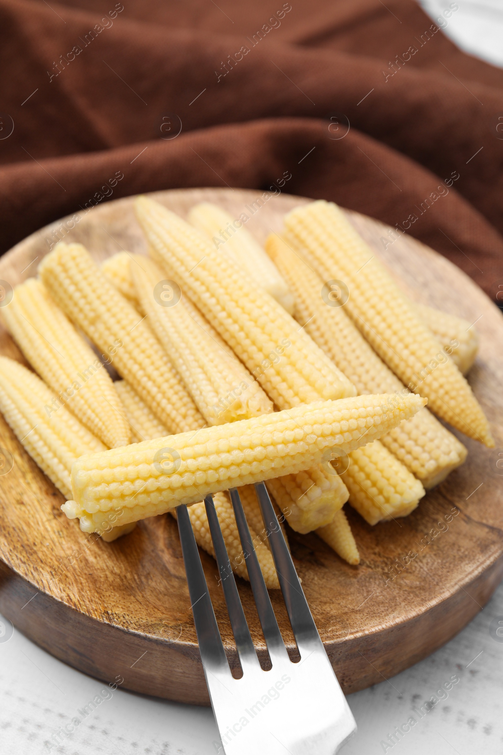 Photo of Pickled baby corn and fork on white wooden table, closeup