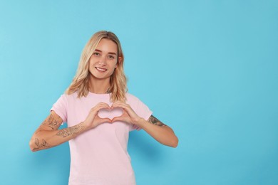Happy volunteer making heart with her hands on light blue background. Space for text