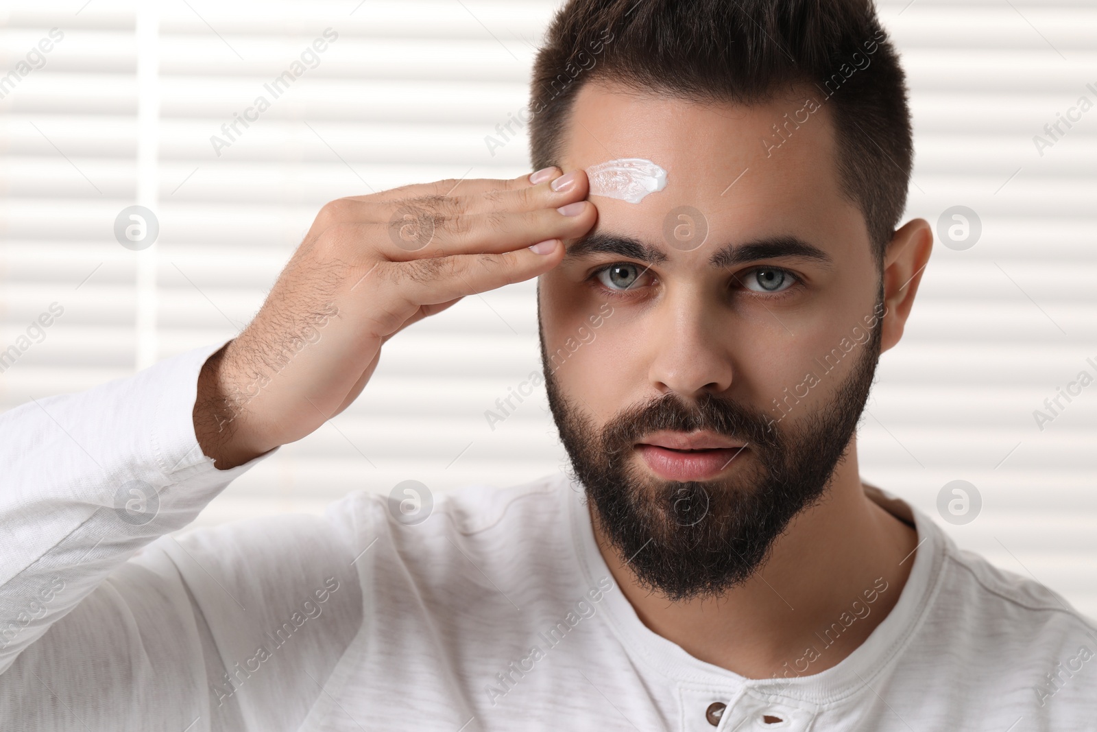 Photo of Man with dry skin applying cream onto his forehead indoors