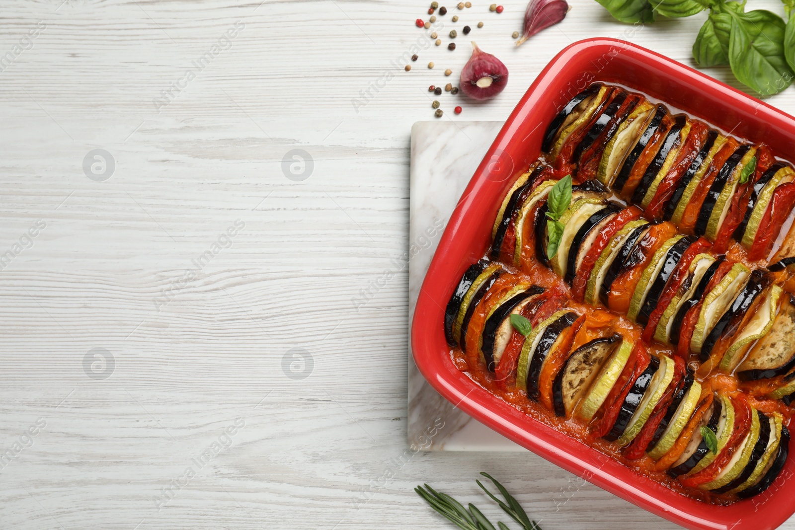 Photo of Delicious ratatouille in baking dish on white wooden table, flat lay. Space for text