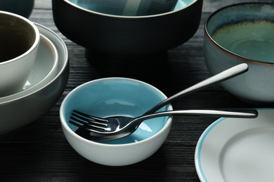 Stylish empty dishware with cutlery on black wooden table