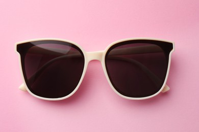 Photo of New stylish elegant sunglasses on pink background, top view