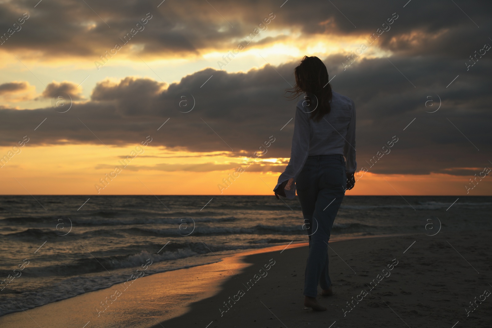 Photo of Woman walking on sandy beach during sunset, back view