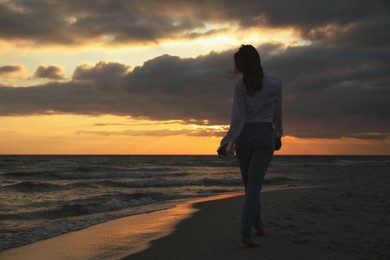 Photo of Woman walking on sandy beach during sunset, back view