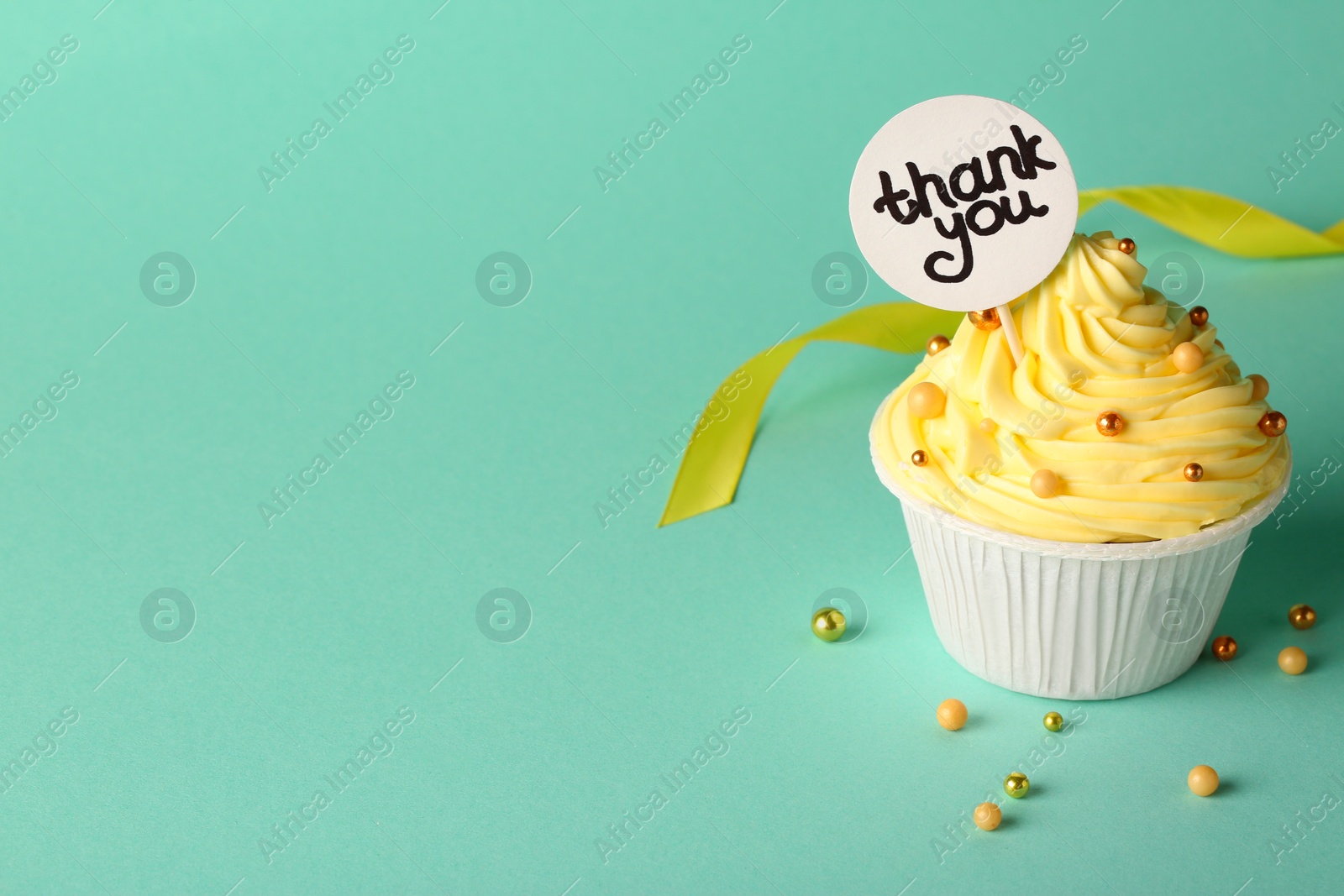 Photo of Tasty cupcake and note with phrase Thank You on turquoise background, space for text