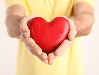 Young man holding wooden heart in his hands on white background, closeup