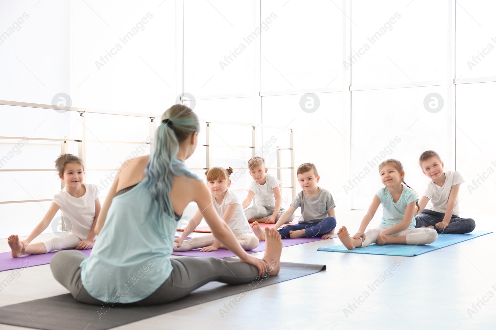 Photo of Little children and their teacher practicing yoga in gym