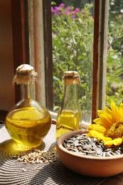 Photo of Bottles of sunflower oil, seeds and flower on table indoors