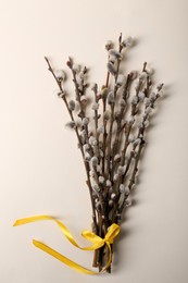 Photo of Beautiful blooming willow branches tied with yellow ribbon on beige background, top view
