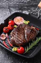Photo of Grill pan with delicious fried beef meat, spices and vegetables on grey textured table