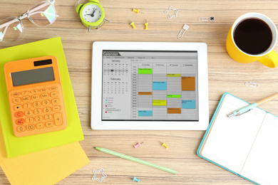 Photo of Modern tablet with calendar app on wooden table, flat lay