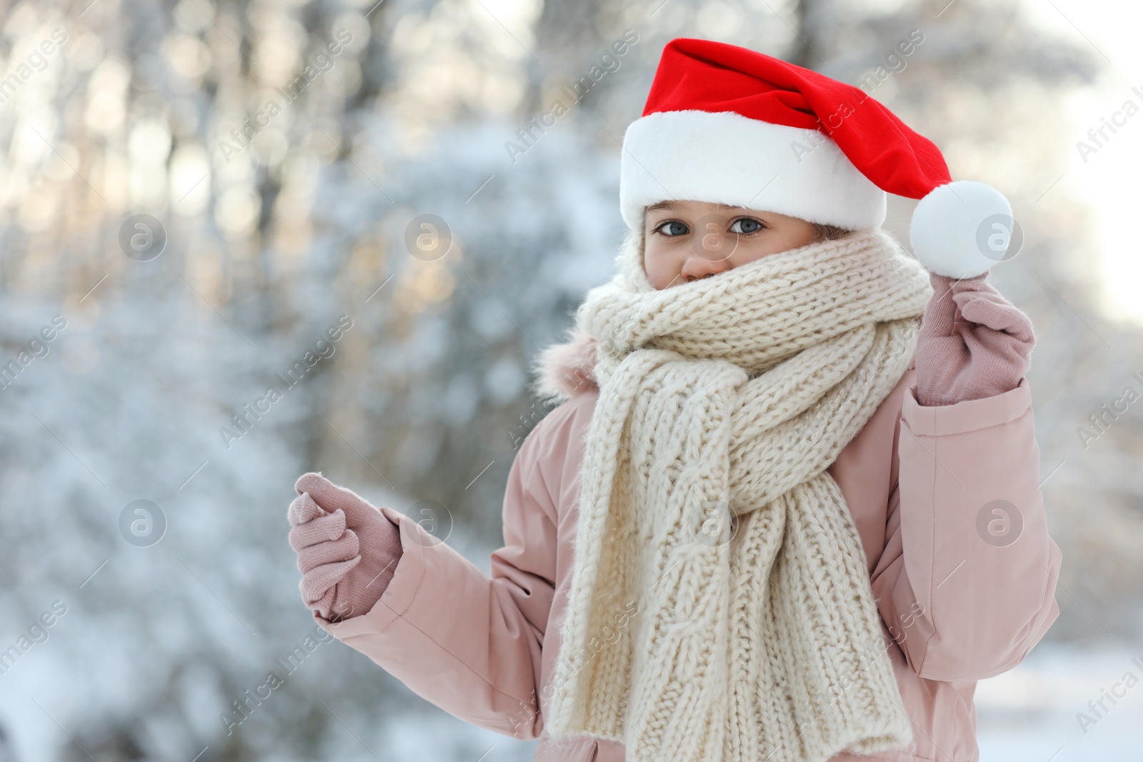 Photo of Cute little girl wearing Santa hat in snowy park on winter day, space for text