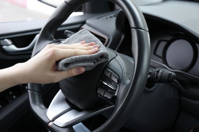 Woman cleaning steering wheel with rag in car, closeup