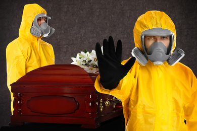 Funeral during coronavirus pandemic. People in protective suits near casket indoors