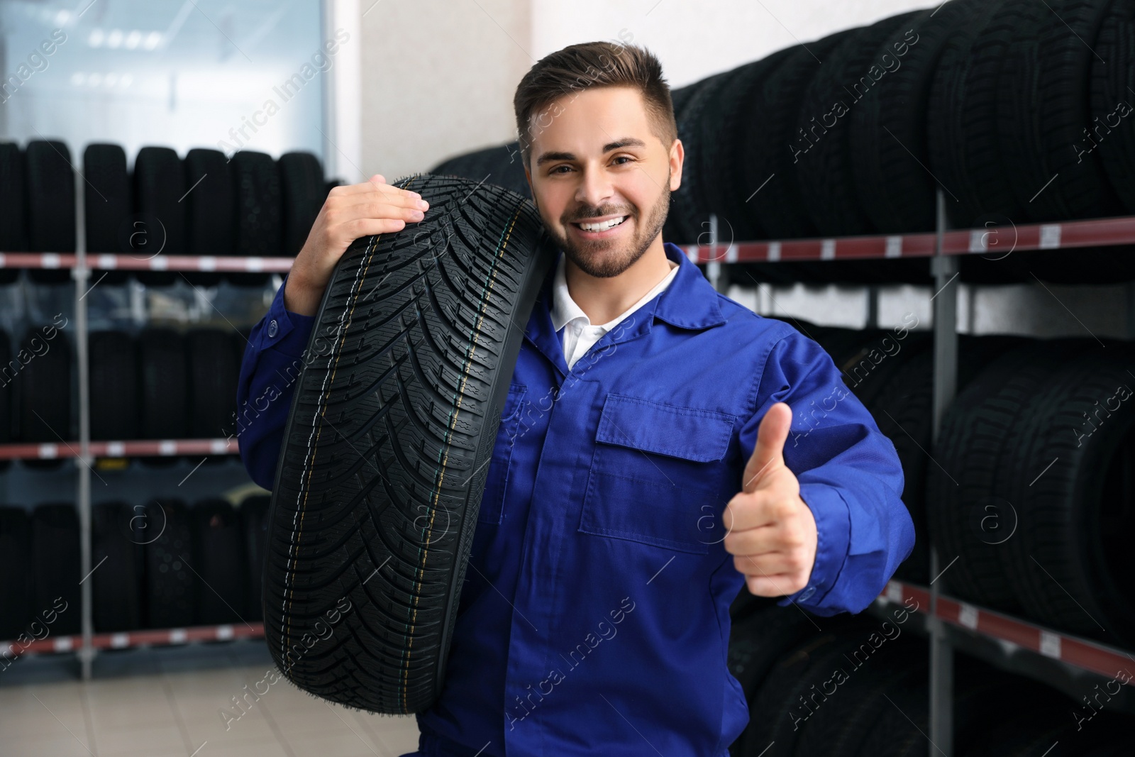 Photo of Male mechanic with car tire in auto store