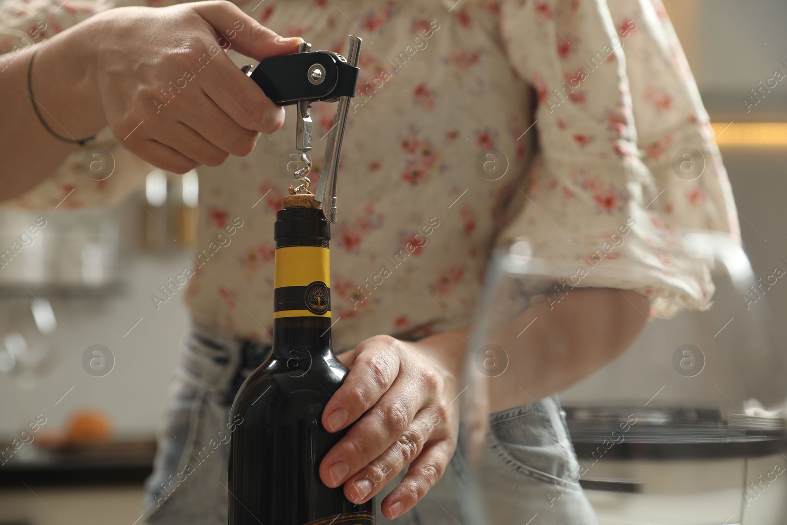 Photo of Woman opening wine bottle with corkscrew on blurred background, closeup