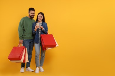 Happy couple with shopping bags and smartphone on orange background. Space for text
