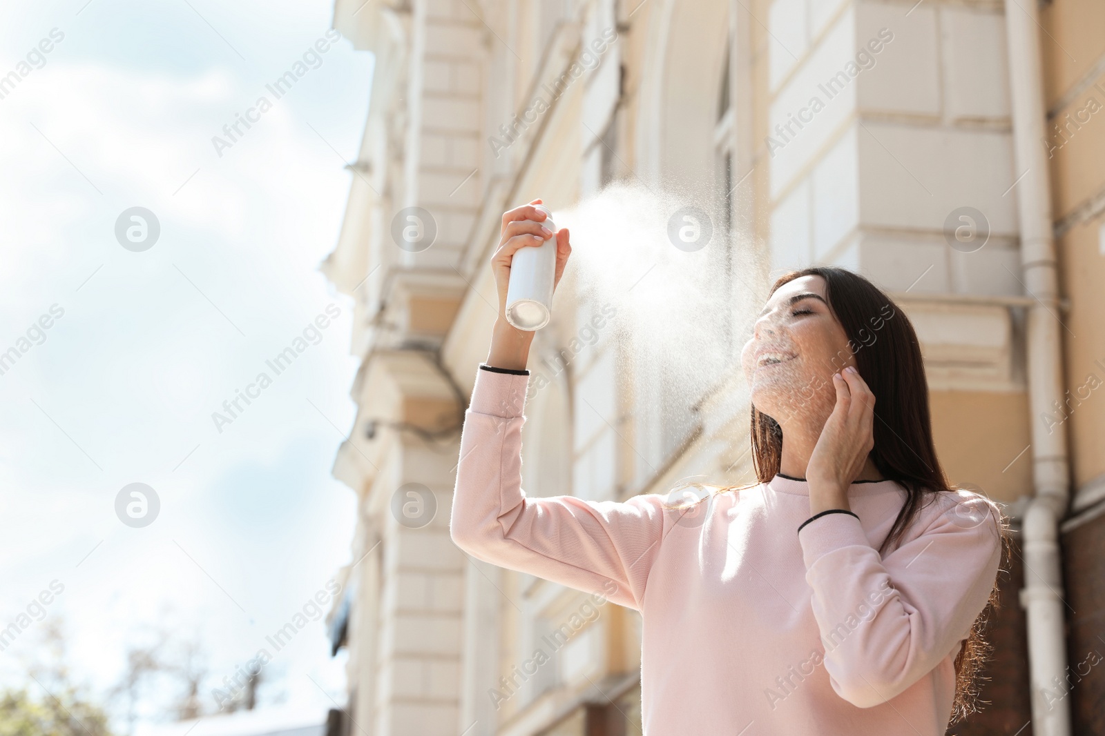 Photo of Young woman applying thermal water on face outdoors, space for text. Cosmetic product