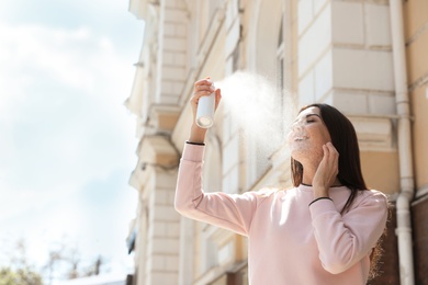 Young woman applying thermal water on face outdoors, space for text. Cosmetic product