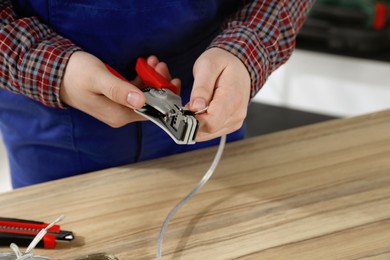 Photo of Professional electrician stripping wiring at wooden table, closeup view