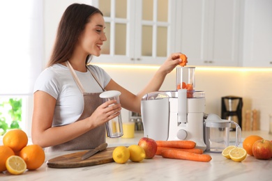 Photo of Young woman making tasty fresh juice at table in kitchen