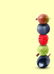 Stack of different fresh tasty berries on honeydew color background, space for text