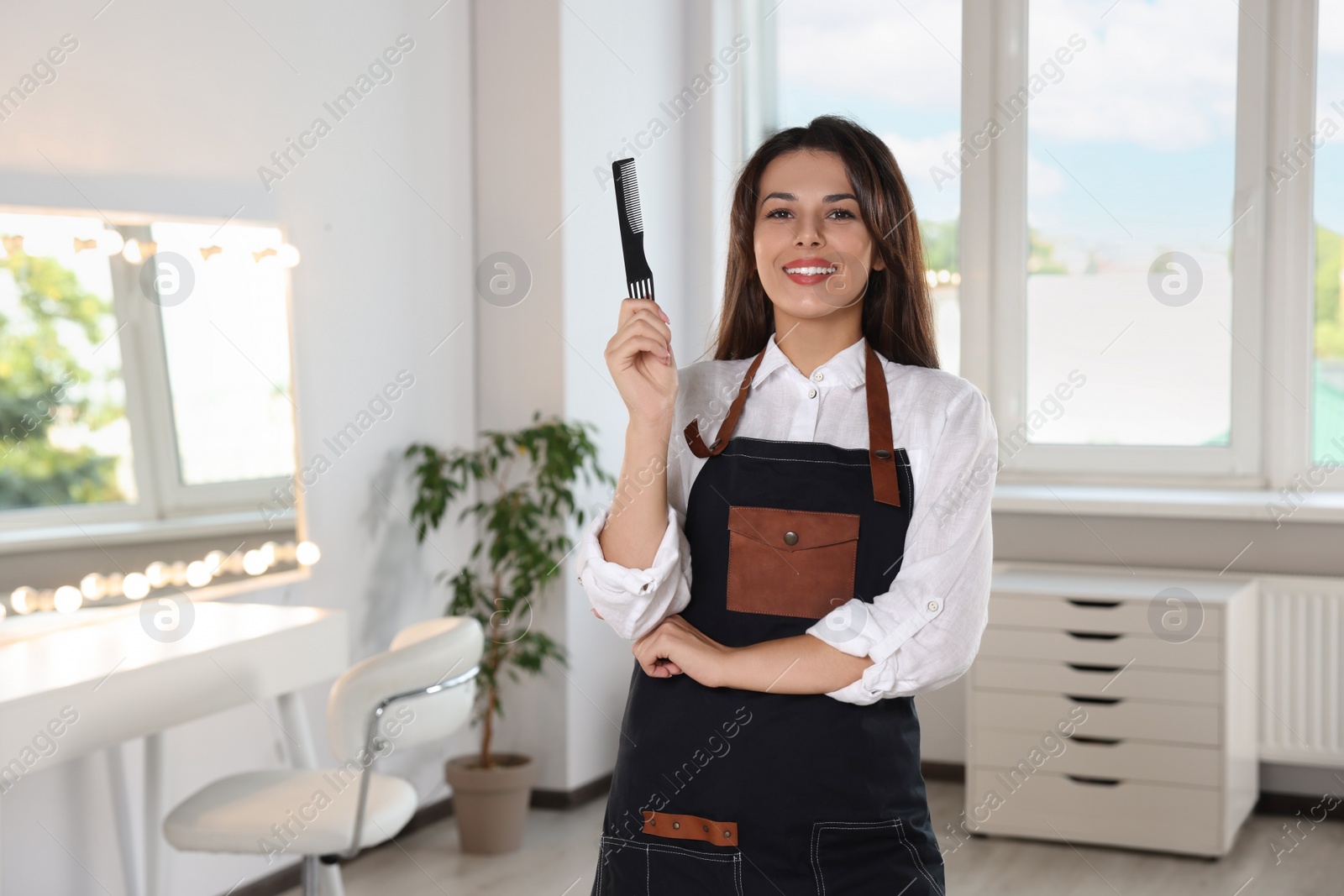 Photo of Portrait of happy hairdresser with professional comb in beauty salon. Space for text