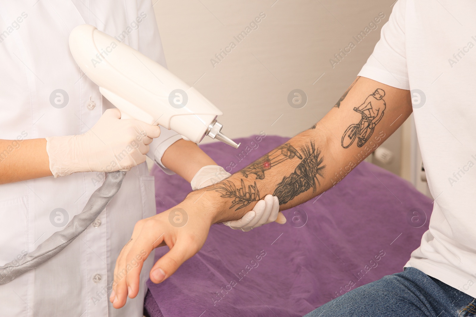 Photo of Young man undergoing laser tattoo removal procedure in salon, closeup