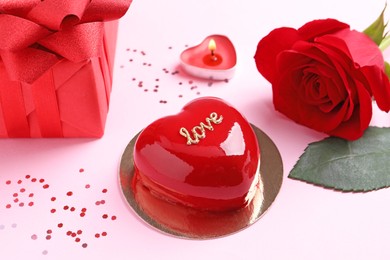 Photo of St. Valentine's Day. Delicious heart shaped cake, gift and rose on light pink background