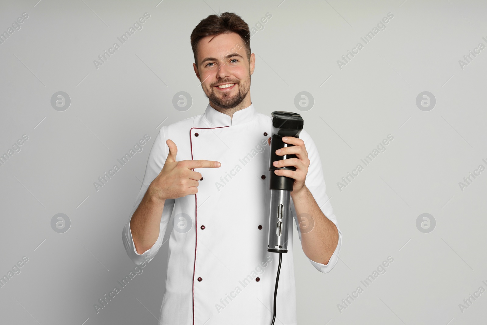 Photo of Smiling chef pointing on sous vide cooker against beige background