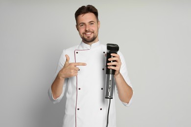 Photo of Smiling chef pointing on sous vide cooker against beige background